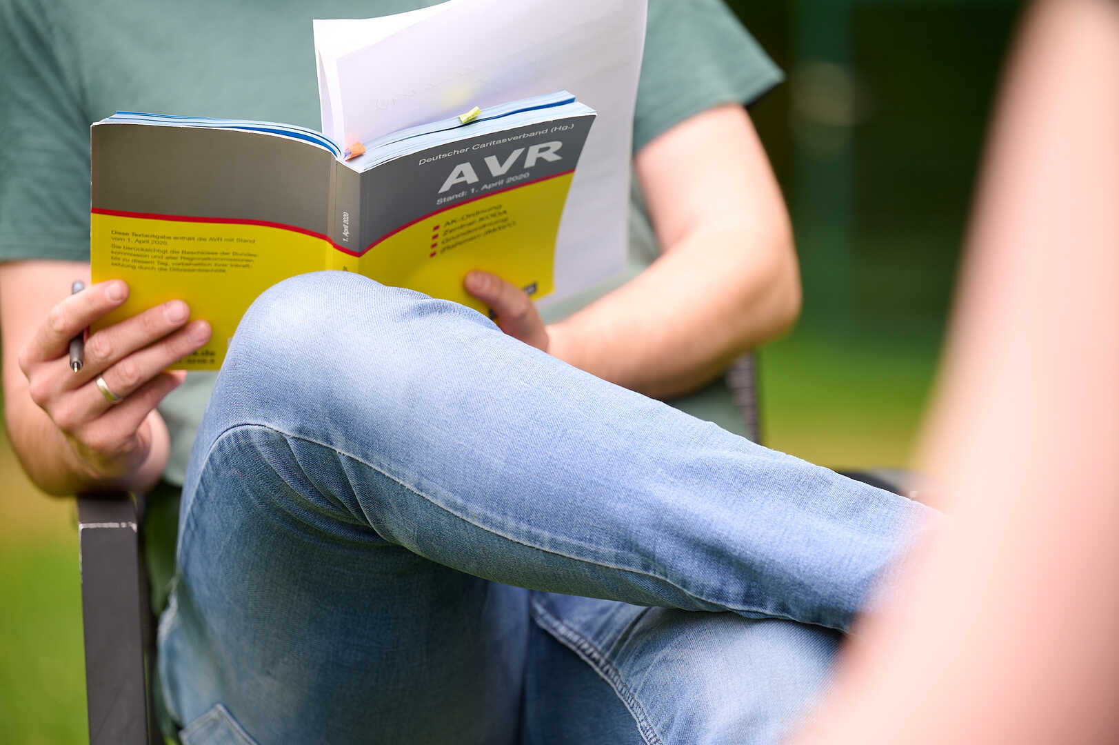 Mann sitzt mit verschränkten Beinen auf einem Stuhl und hält ein Buch mit der Aufschrift AVR in der Hand